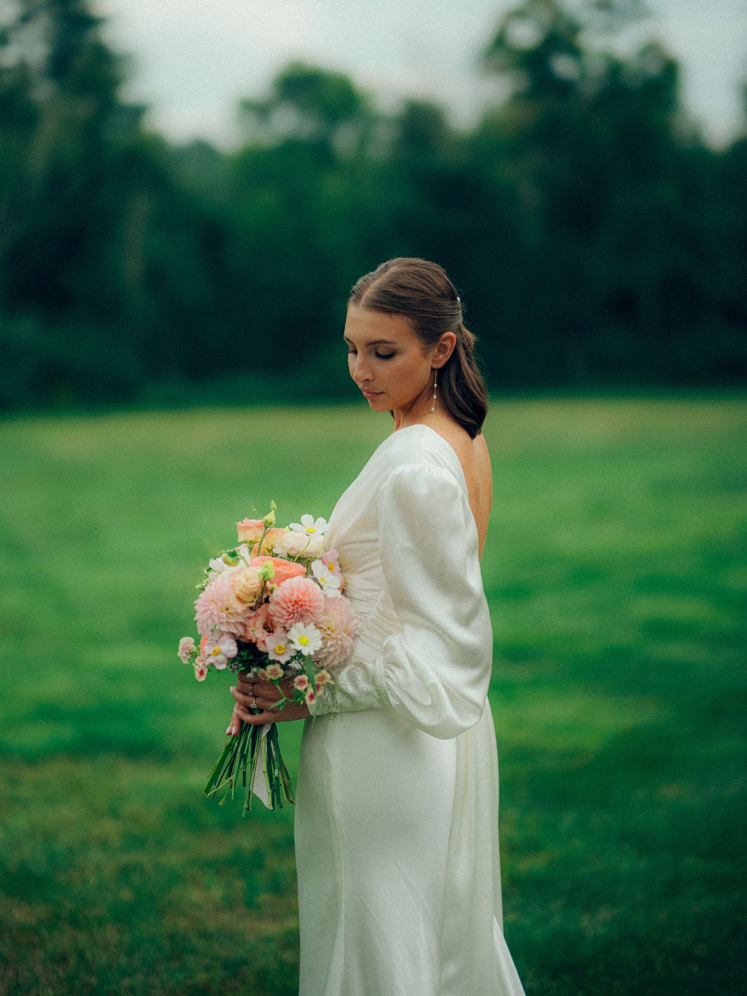 Bride in elegant white dress holds beautiful bouquet of pink and peach flowers in a garden setting.