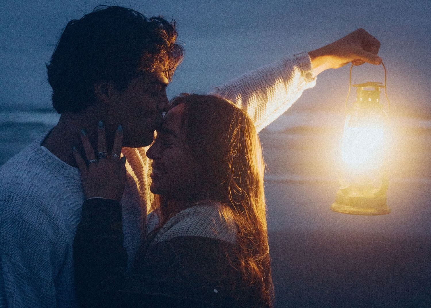 A couple shares an intimate moment in the dark while holding up a glowing lantern against the night sky.