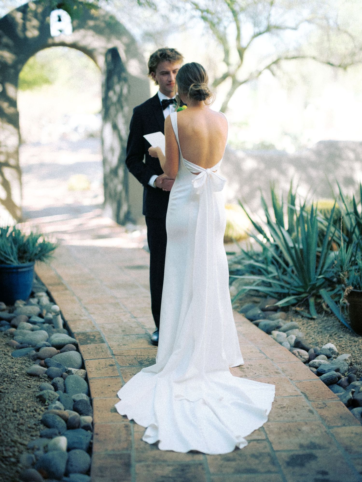 An elegant backlit wedding couple standing on a stone path surrounded by desert plants.