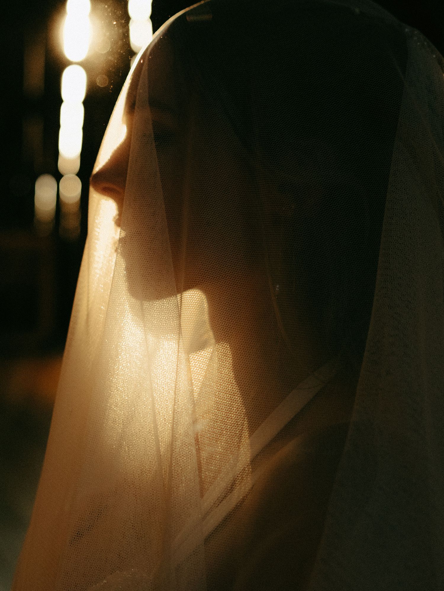 Ethereal side profile silhouette with veil backlit by warm glowing light.
