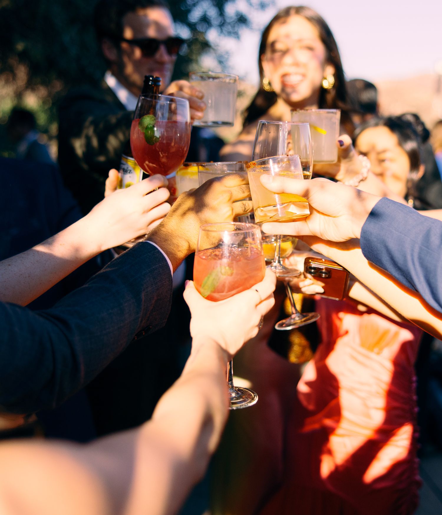 Friends raise colorful cocktail glasses in a celebratory toast during sunset.