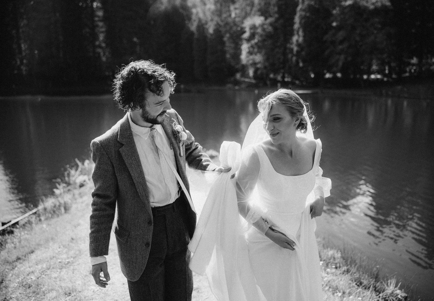 A candid wedding photo of newlyweds laughing together by a serene lake.