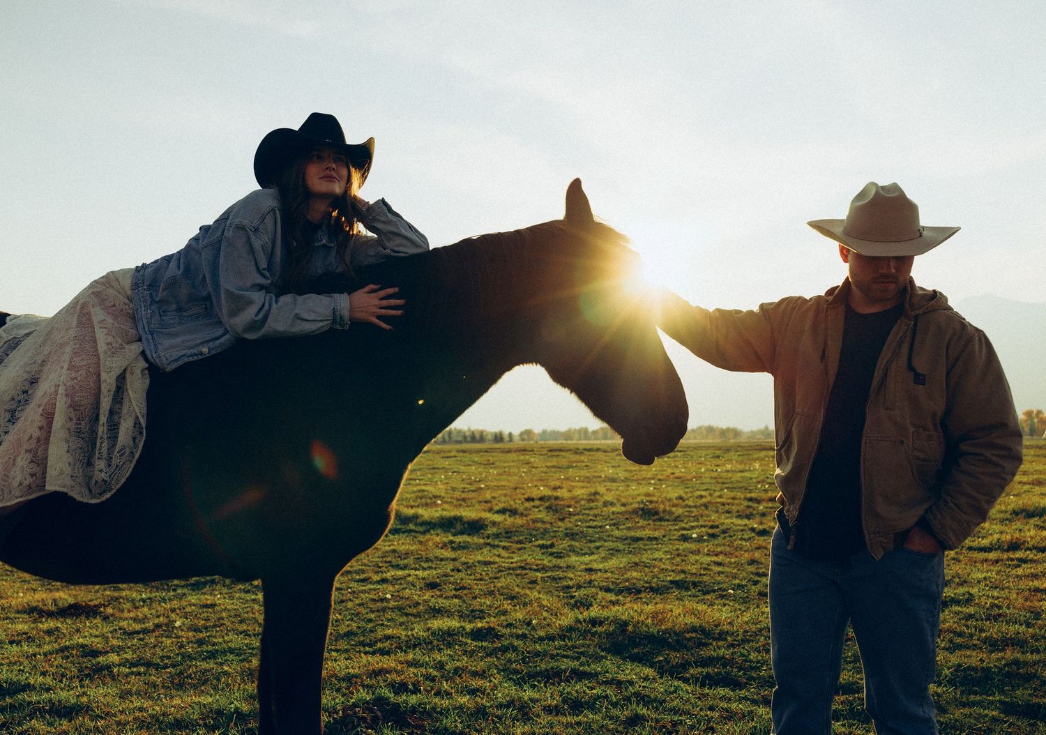 Two people with a horse at sunset in a pastoral field setting.