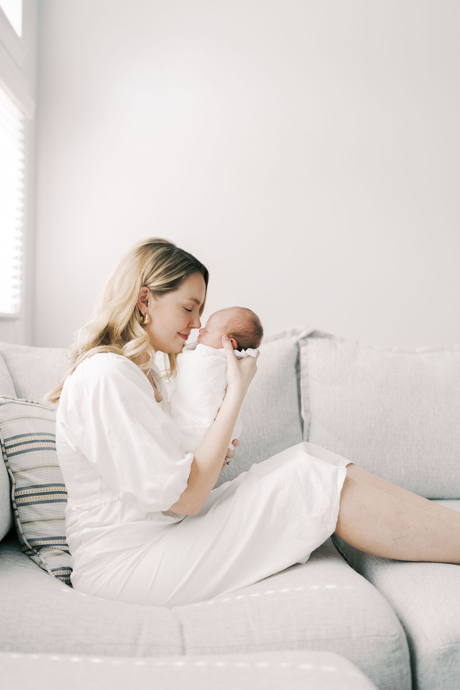 Woman in white lounges peacefully on light gray couch in minimalist setting.