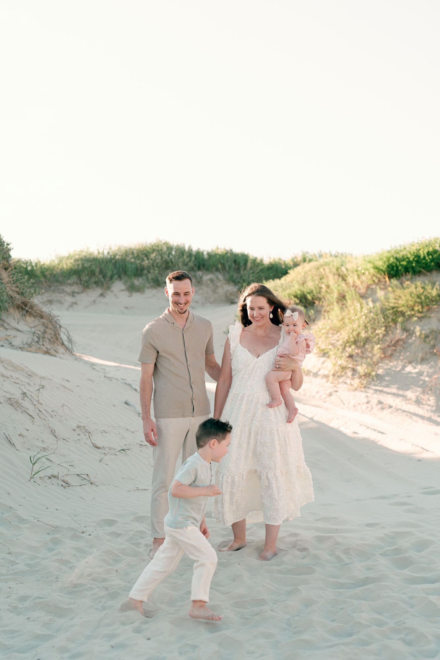 Family walking together on sand dunes during a beach photoshoot.