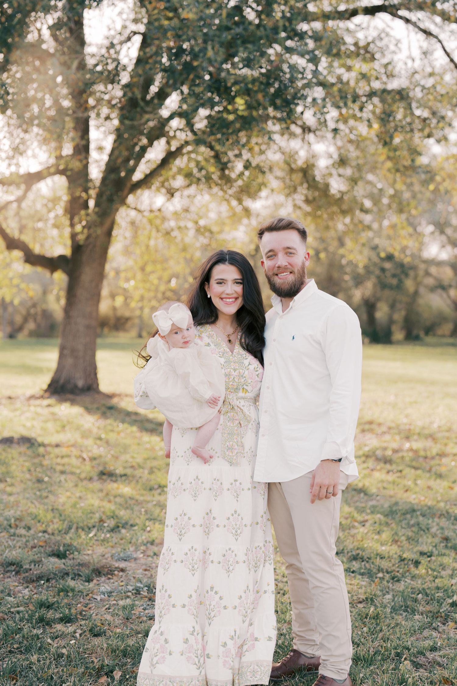 Family dressed in cream colored outfits posing under autumn tree.