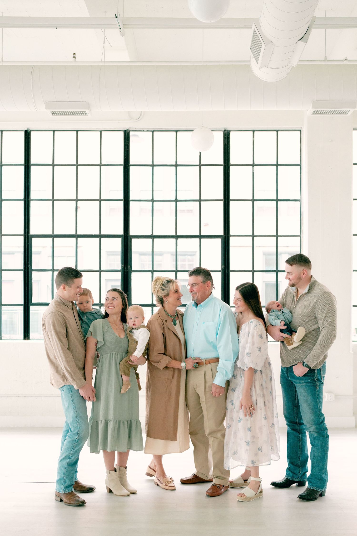 Multi-generational family group portrait in bright modern studio with large windows.