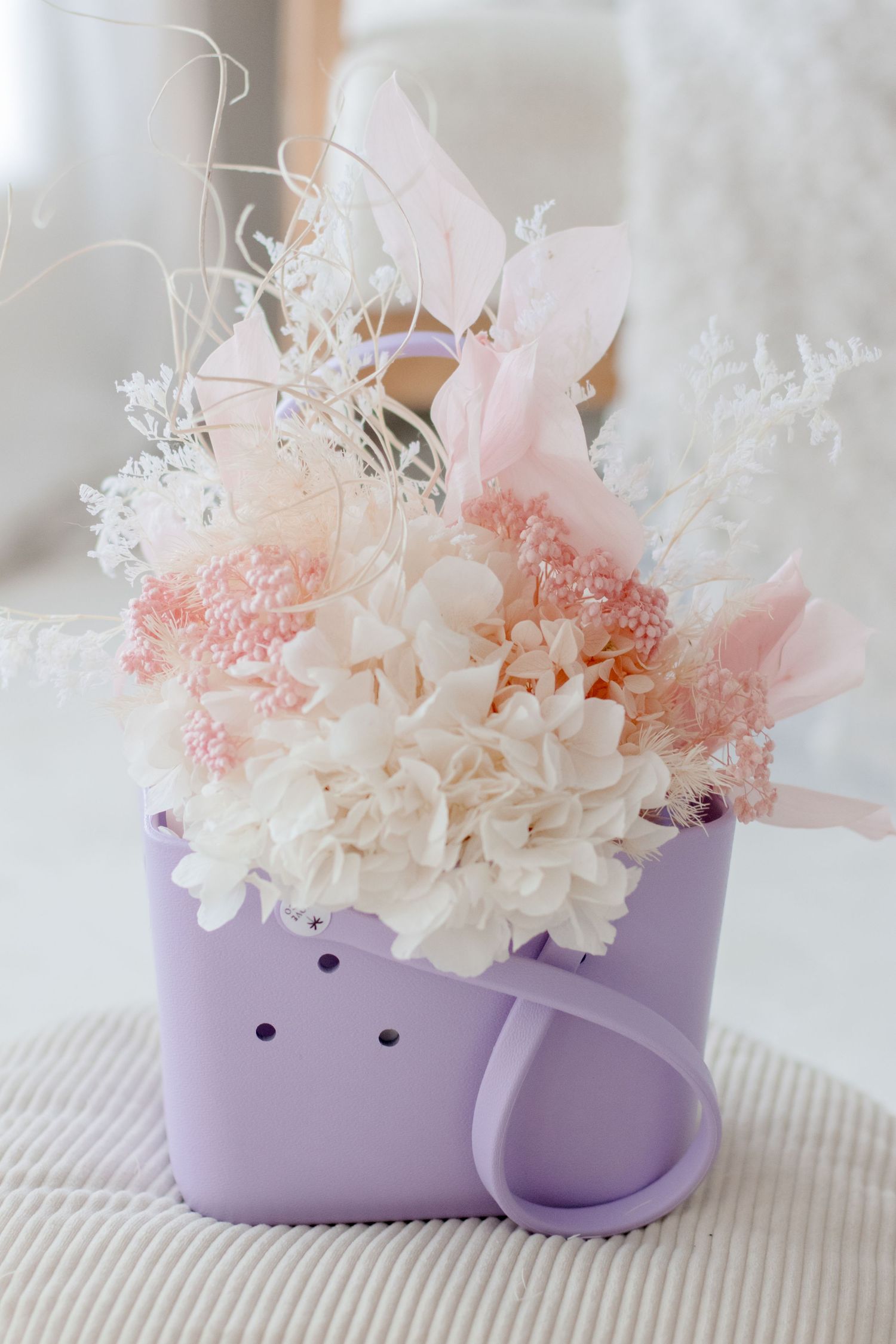 Pink and white dried flowers arranged in purple ceramic mug.