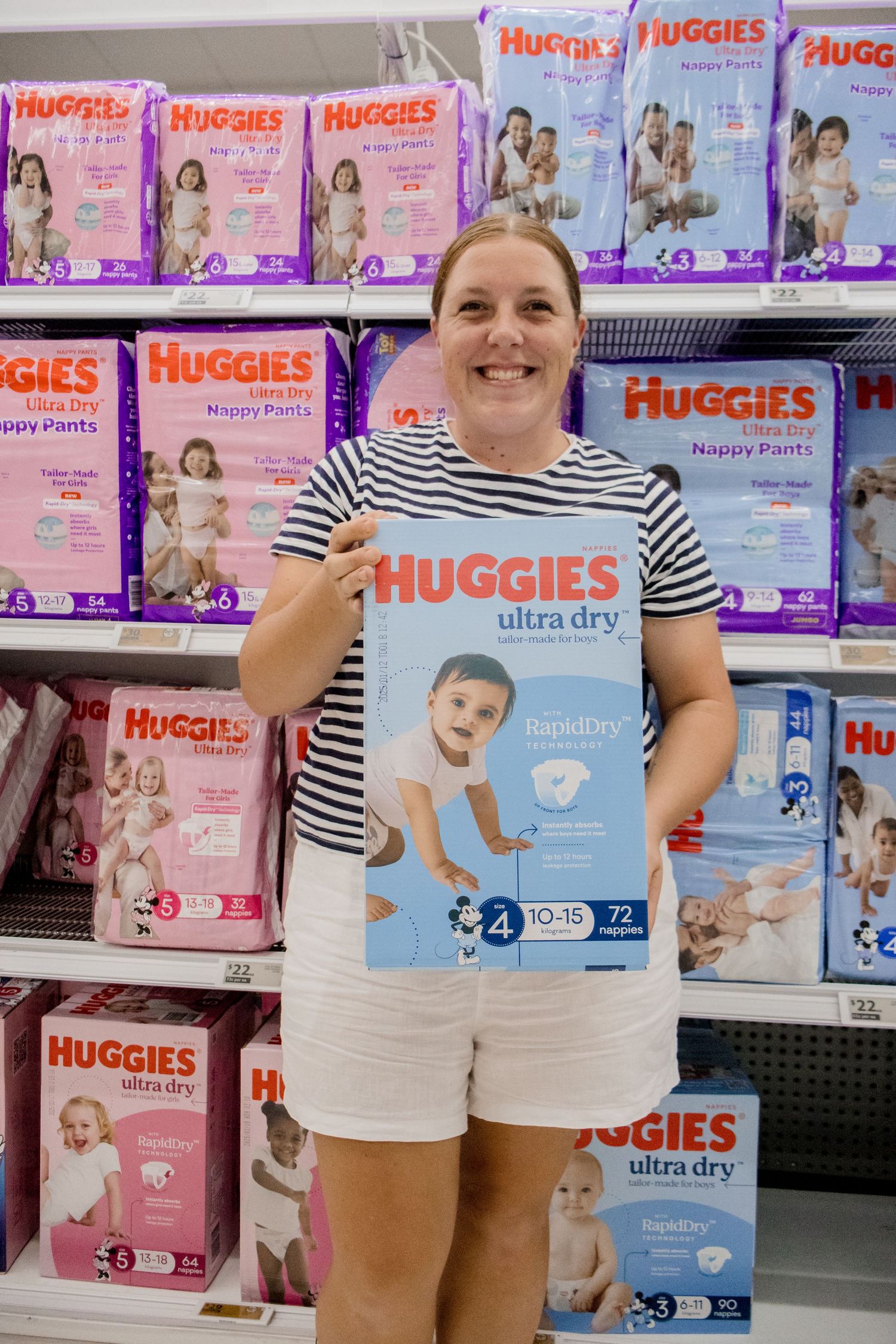 Customer in striped shirt shops for Huggies diapers in store aisle with colorful diaper packages displayed on shelves.