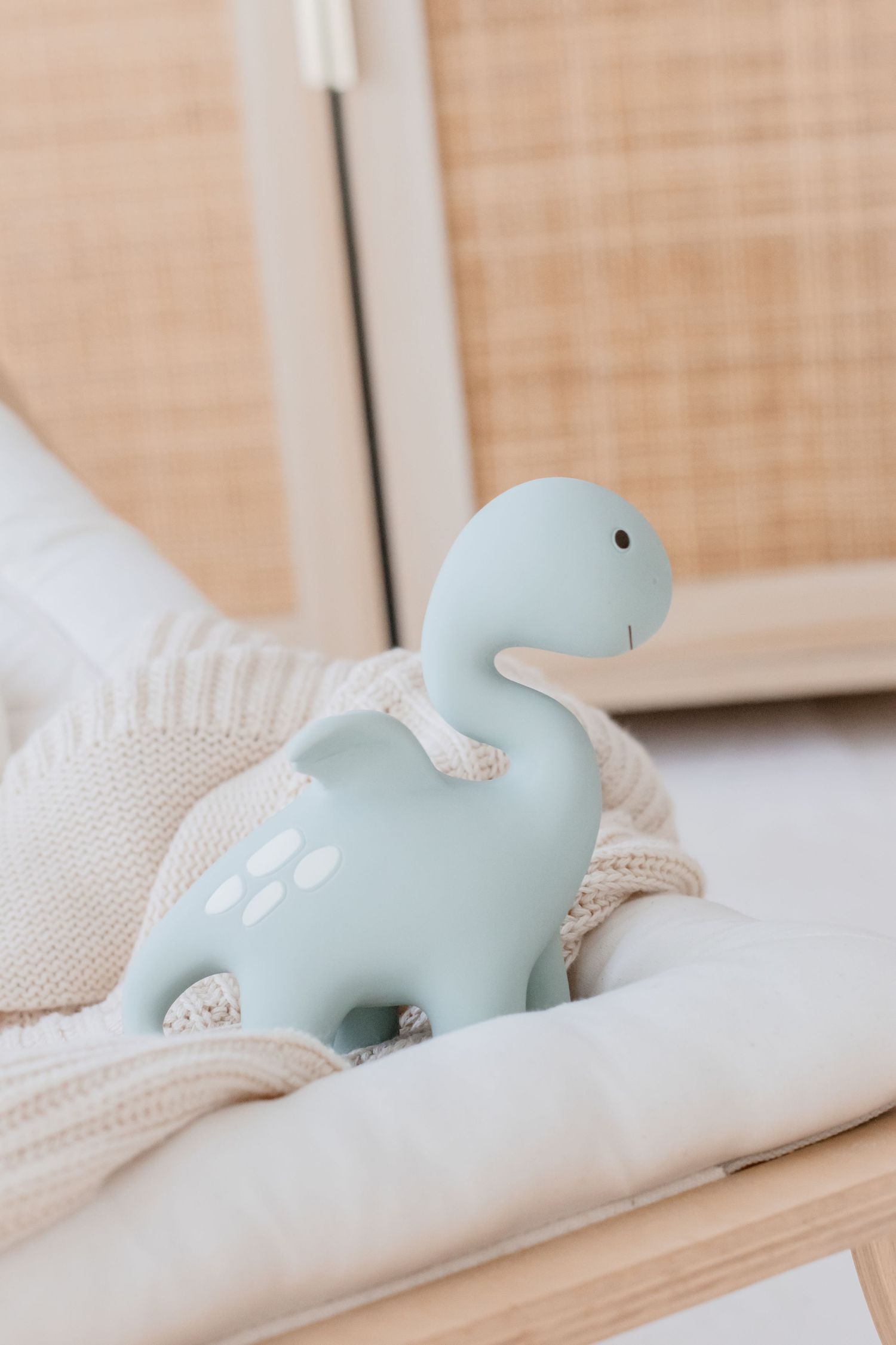 Light blue dinosaur toy rests on cream knitted blanket.