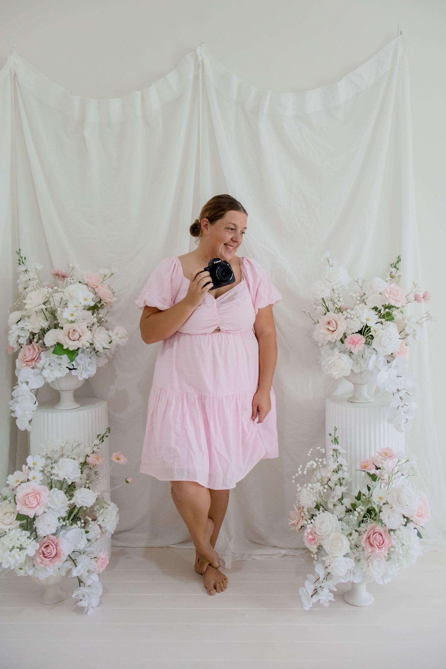 Portrait session with floral arrangements and white backdrop.