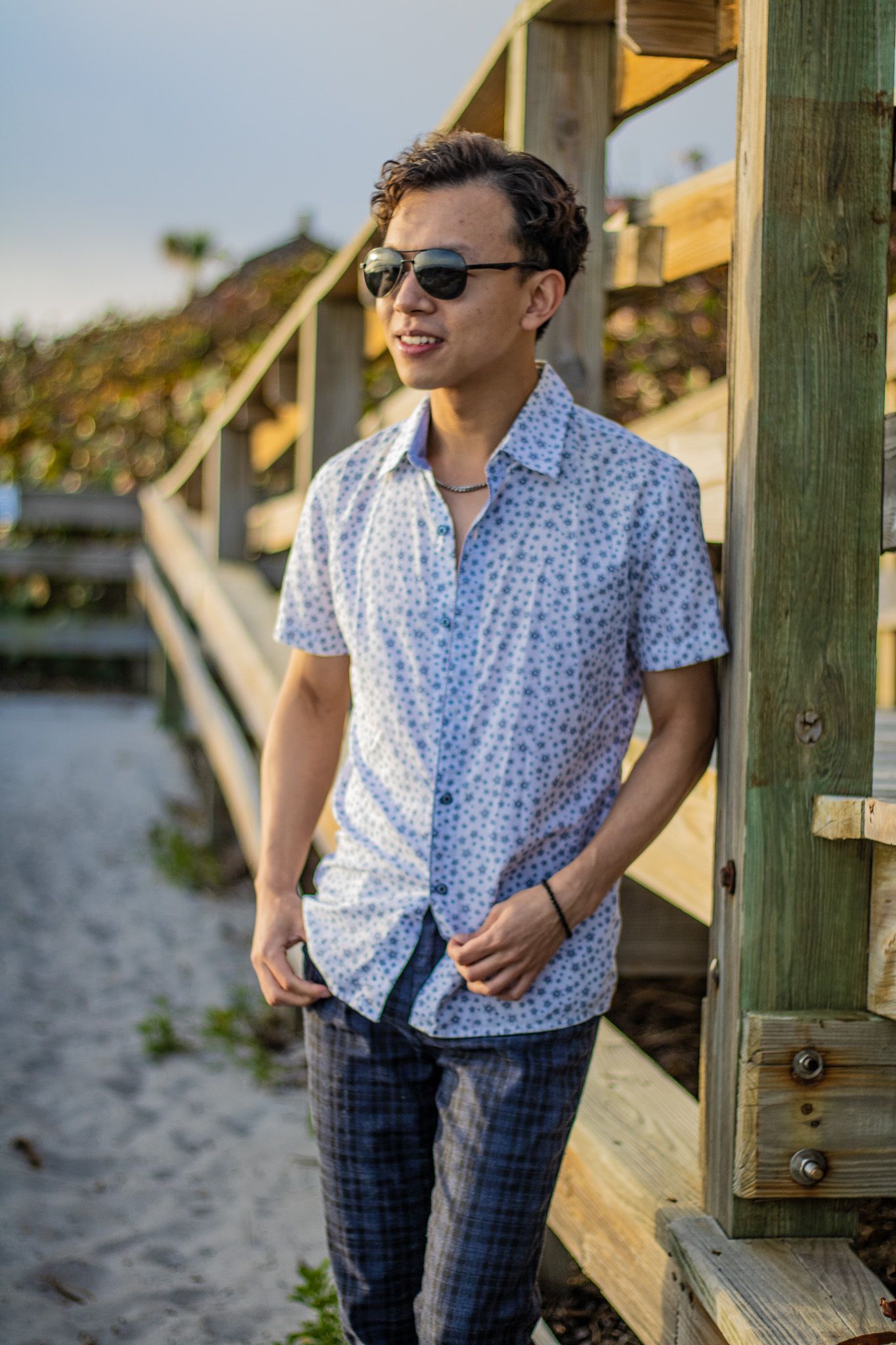 Sunny beach portrait with sunglasses and casual summer attire by wooden stairs.