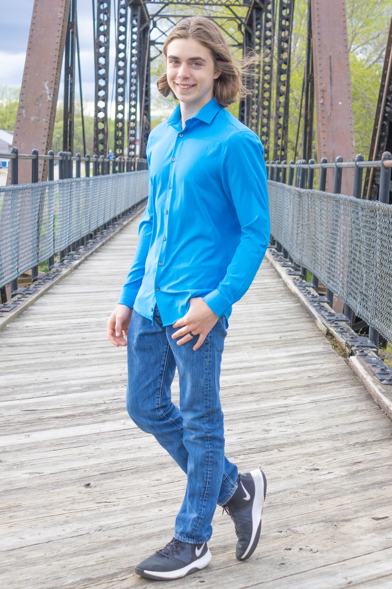 Person in vibrant blue button-down walks along rustic bridge walkway.