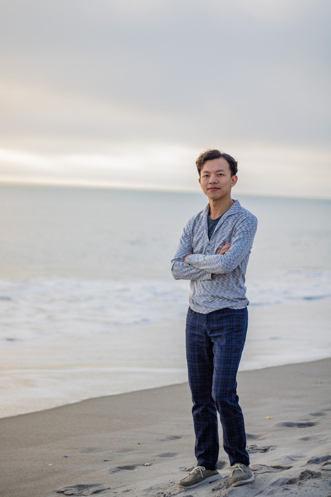 Portrait of someone on beach with arms crossed against overcast sky.