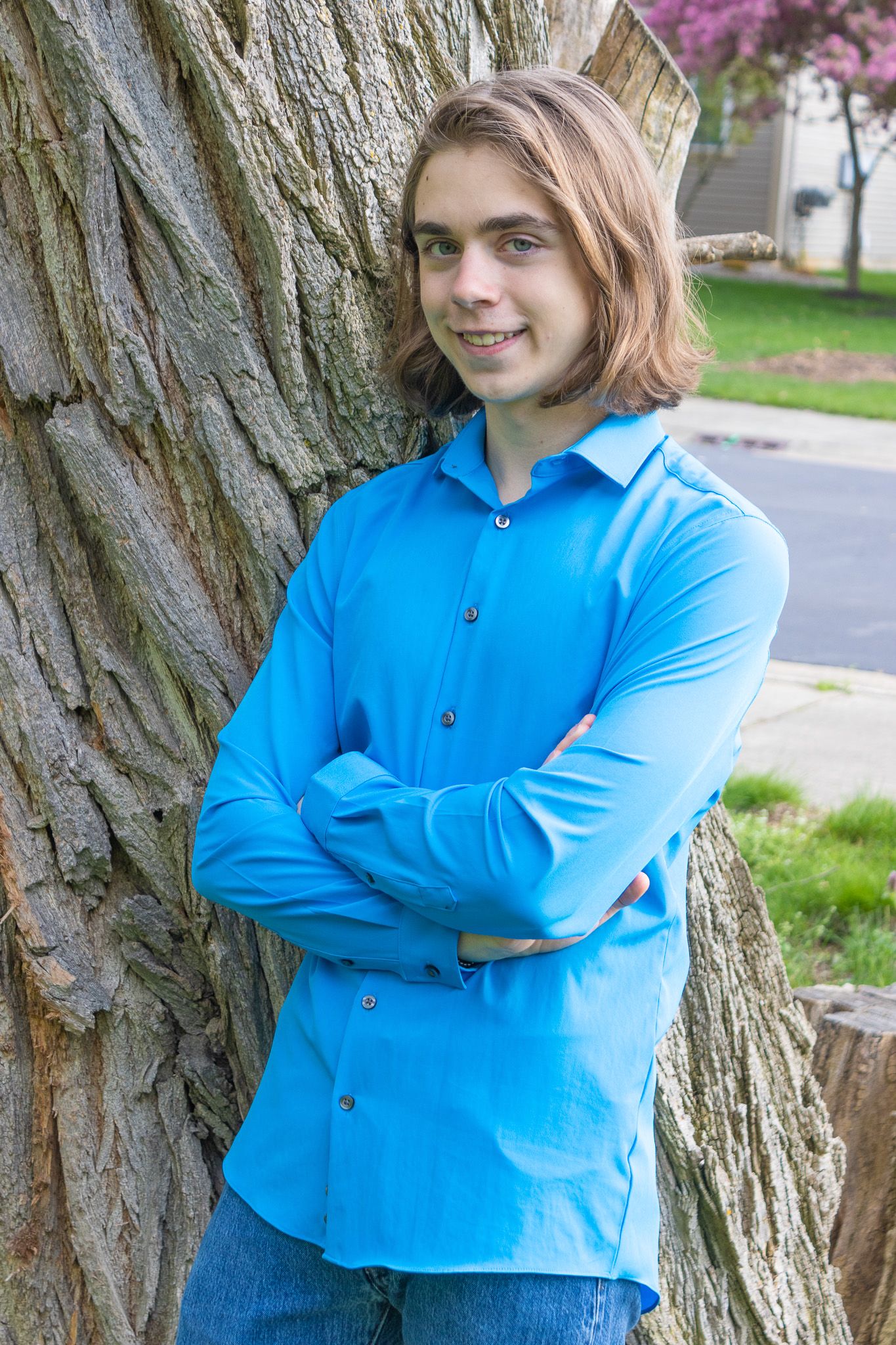 Person in bright blue shirt leans against large tree trunk outdoors.