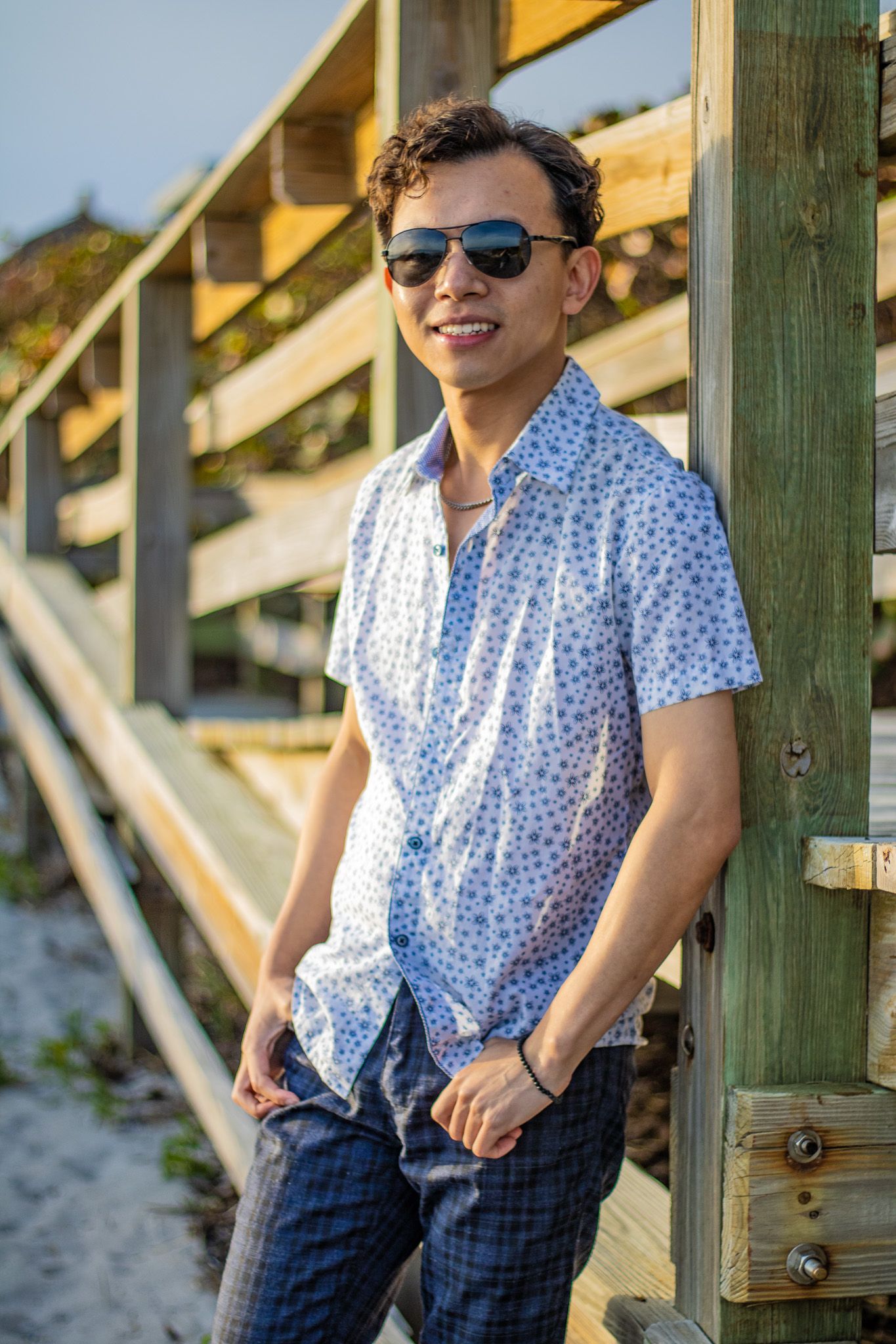 Casual beachwear portrait with sunglasses and patterned shirt against wooden railings.