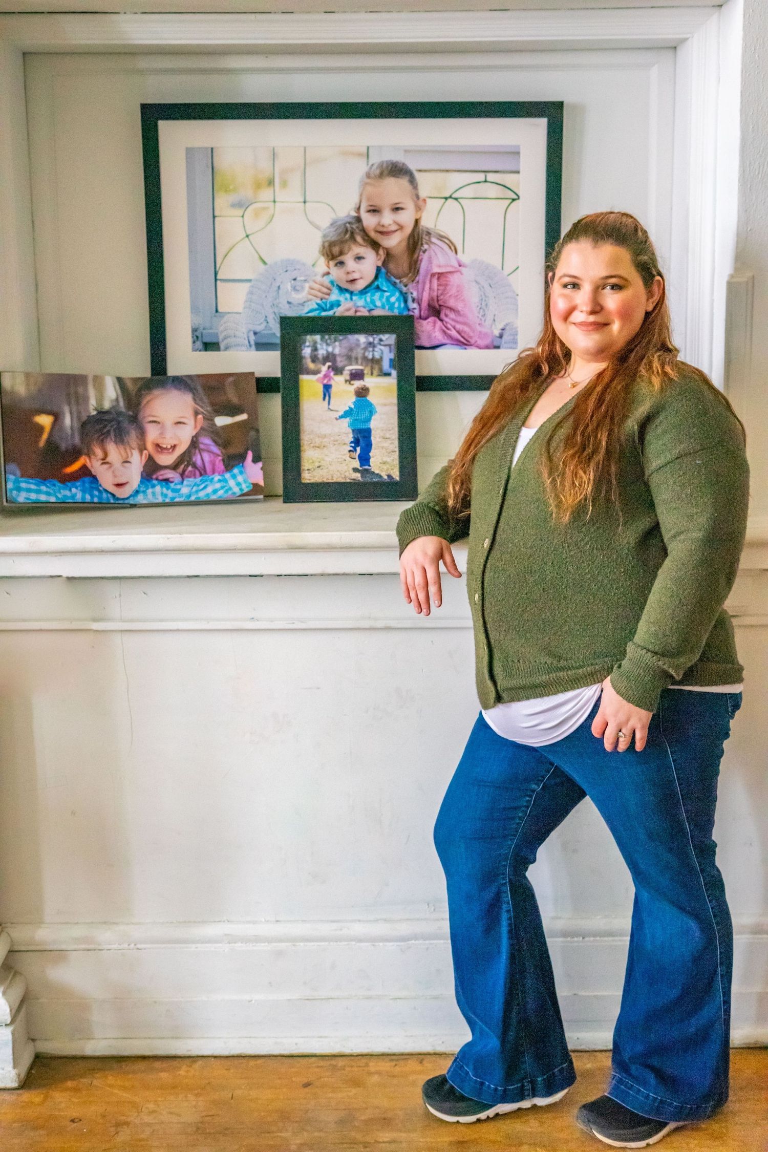 A person in green poses next to a wall displaying framed family photographs.