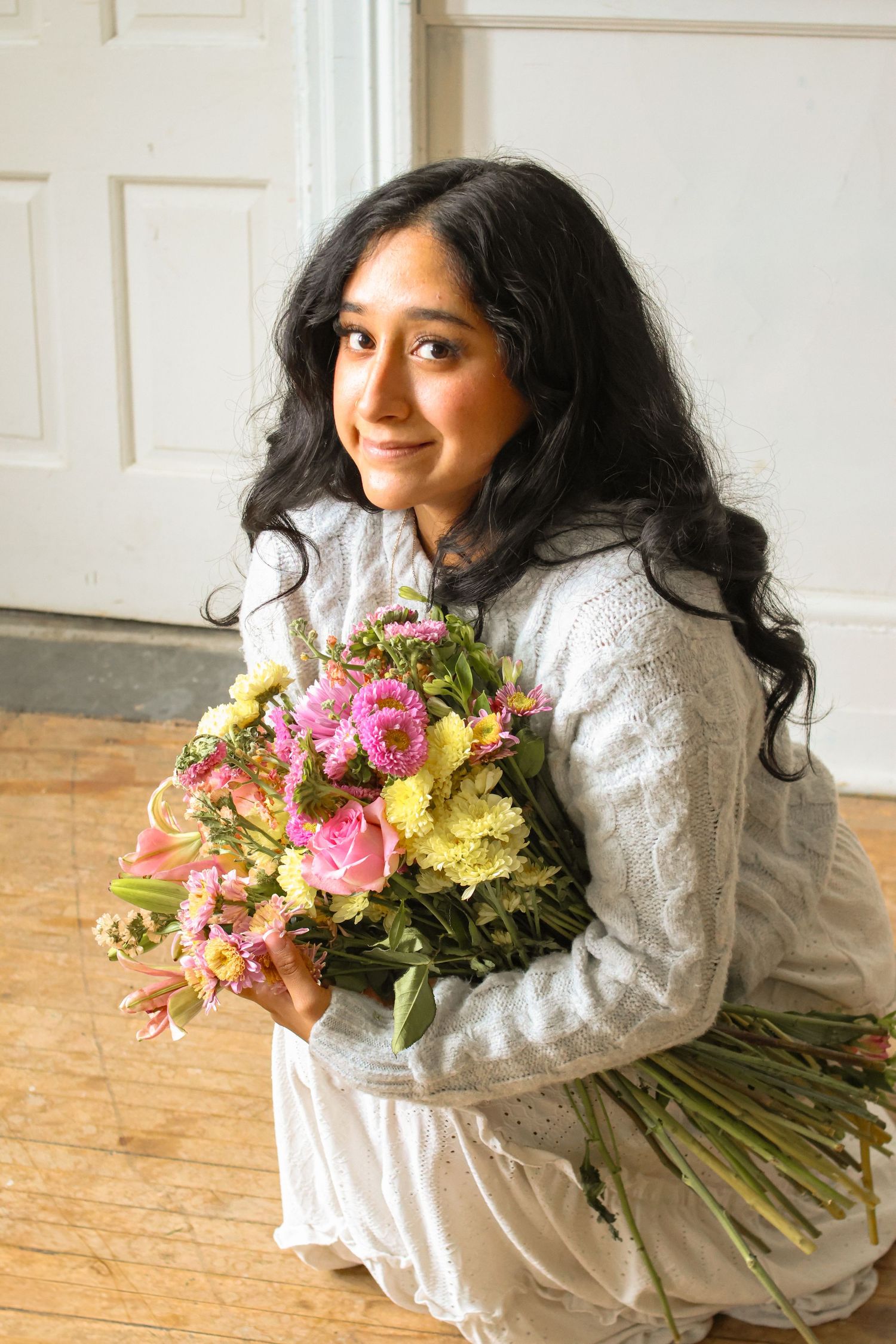 Person in white dress holding colorful floral bouquet against paneled wall.