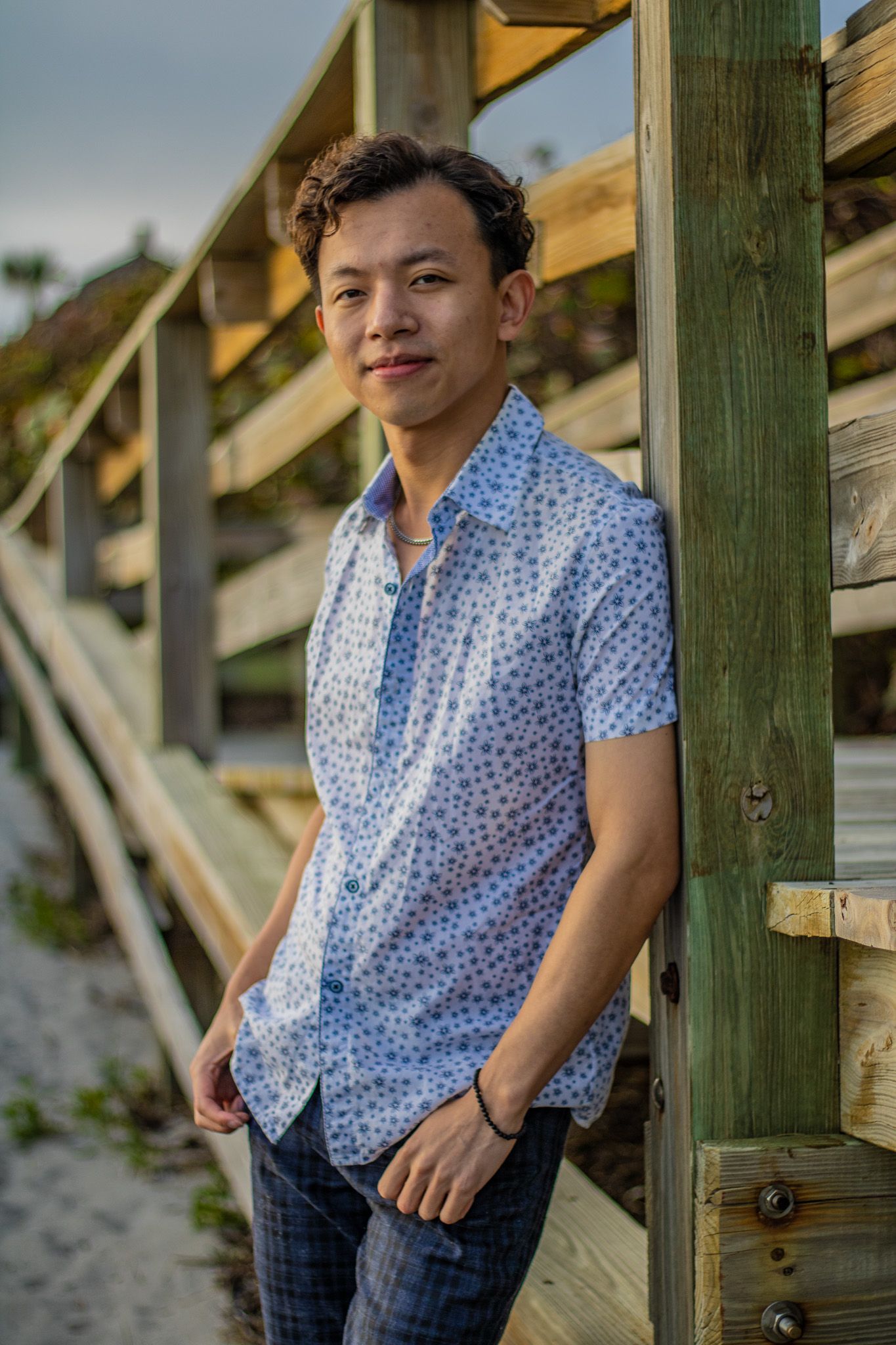Summer fashion portrait on beach boardwalk wearing blue patterned shirt at golden hour.