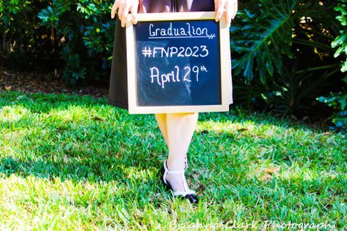 Graduation announcement chalkboard showing FNP 2023 date held in garden setting.