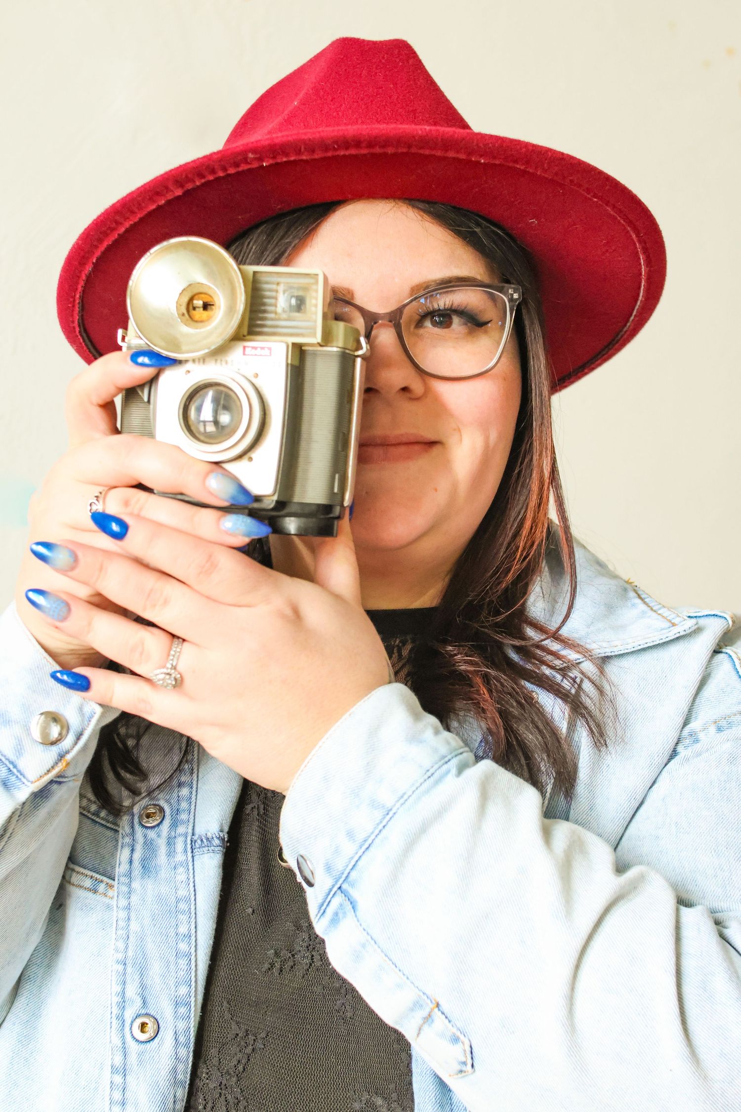 Person wearing red hat and denim jacket holding vintage camera.