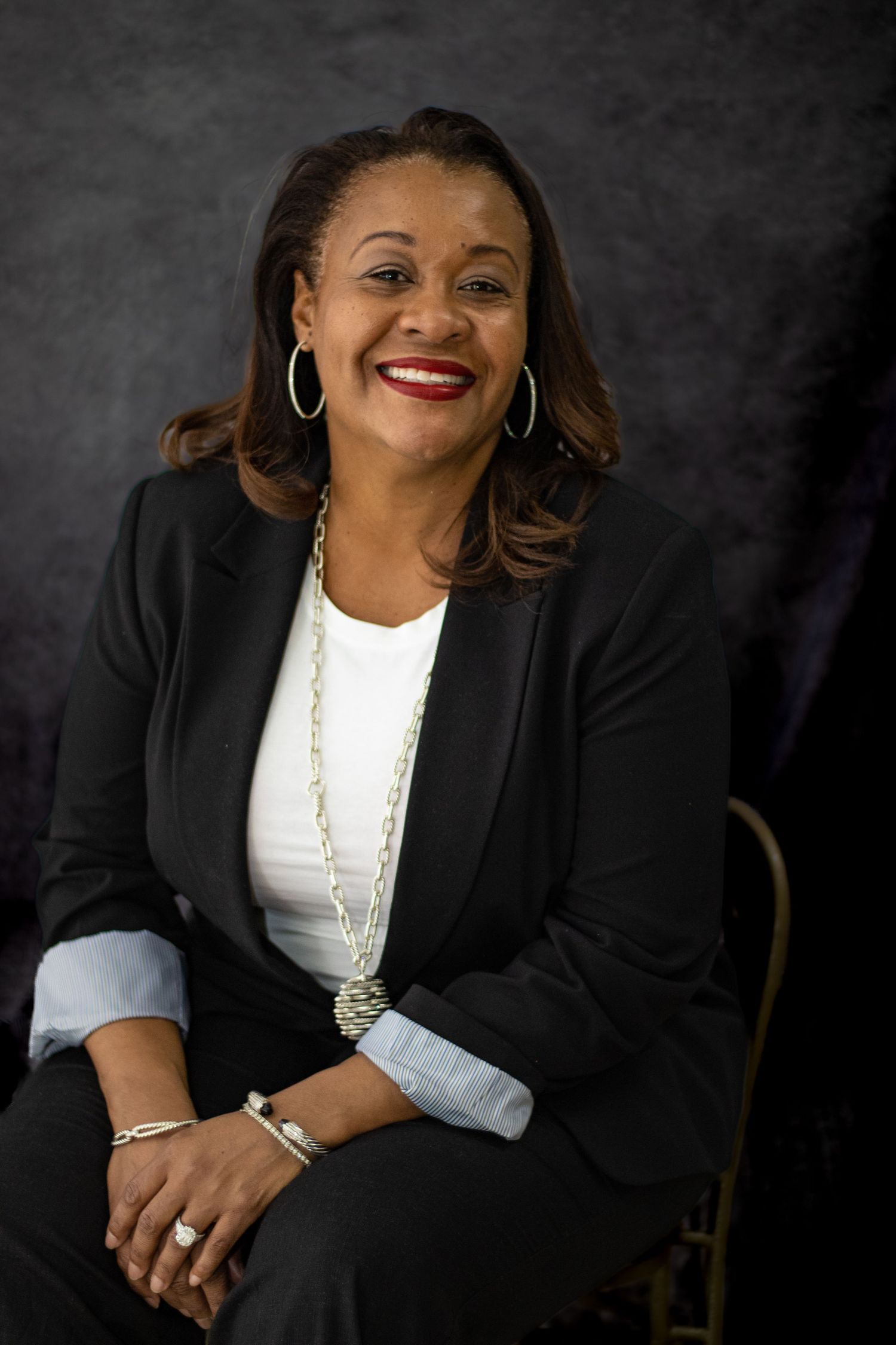 Studio portrait showing confident pose in black blazer and white top with accessories.