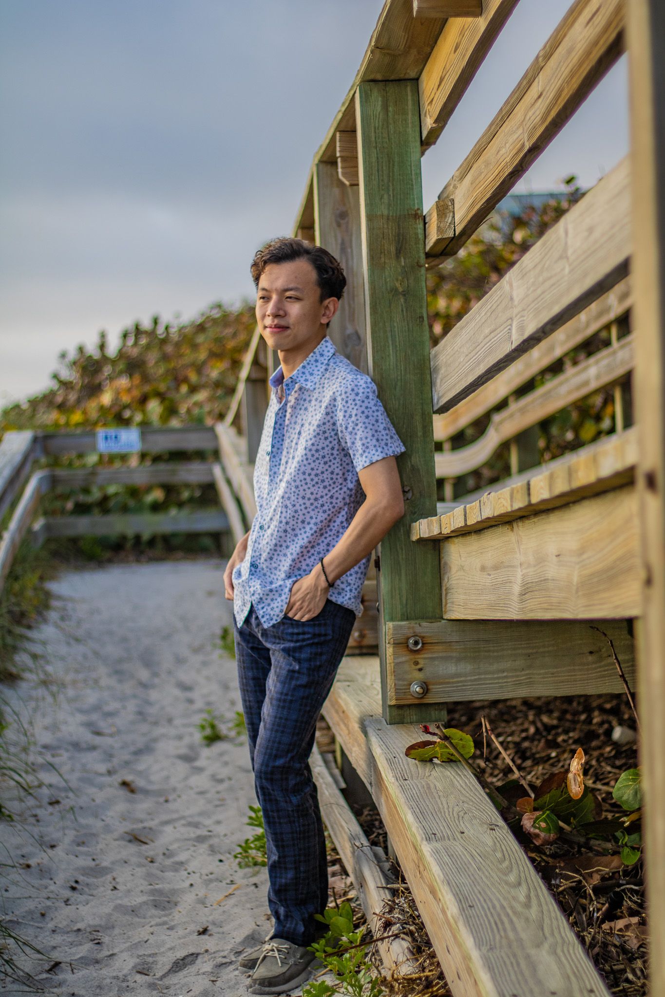 A beachwear fashion shot featuring a floral shirt and dark jeans on wooden steps by the sand.