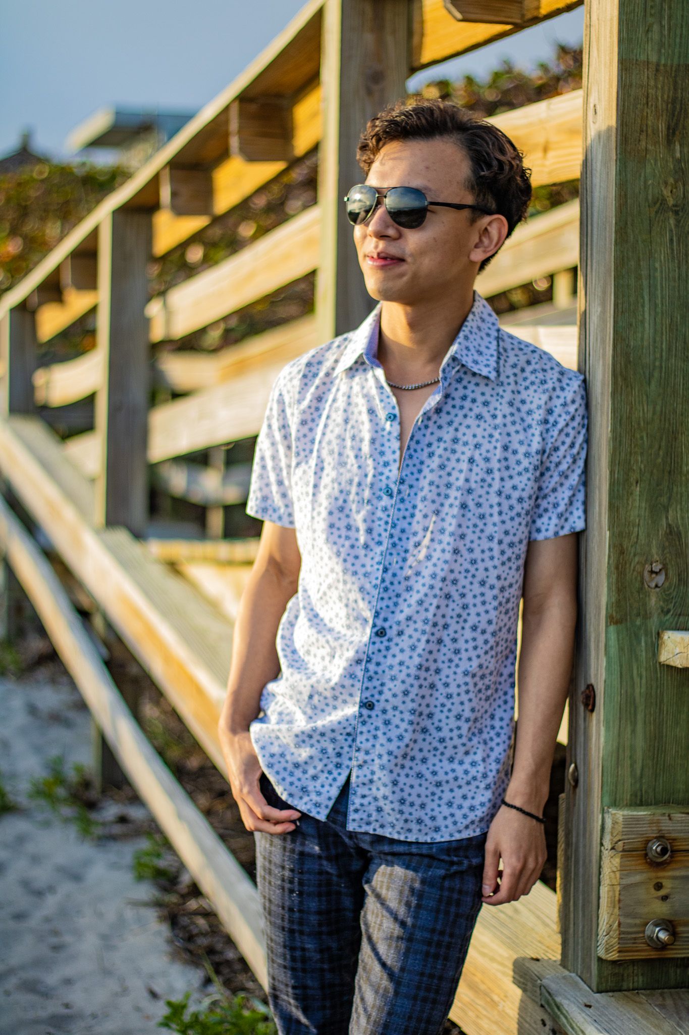 Relaxed coastal fashion shot featuring sunglasses and patterned shirt on beach walkway.