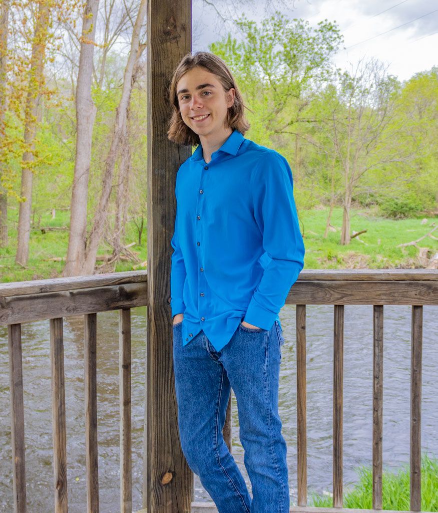 Person in bright blue sweater stands on wooden deck overlooking water surrounded by autumn trees.