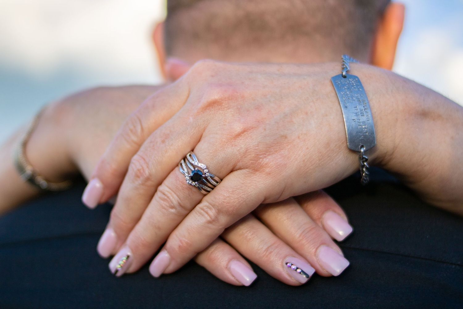 Close up of engagement ring and manicured hands against dark clothing.