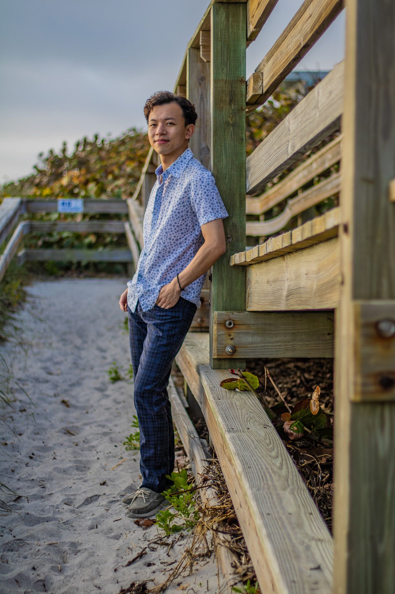 Casual portrait against a wooden beach stairway with sand and coastal vegetation.