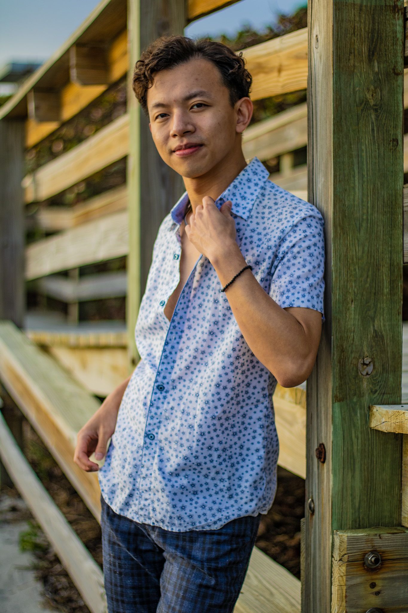 Stylish casual beach portrait with floral shirt against wooden walkway structure.