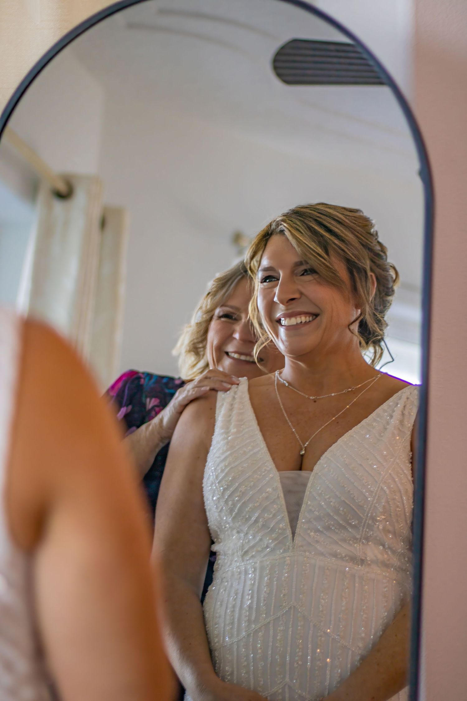 Mirror reflection shows person in white beaded wedding dress getting ready.