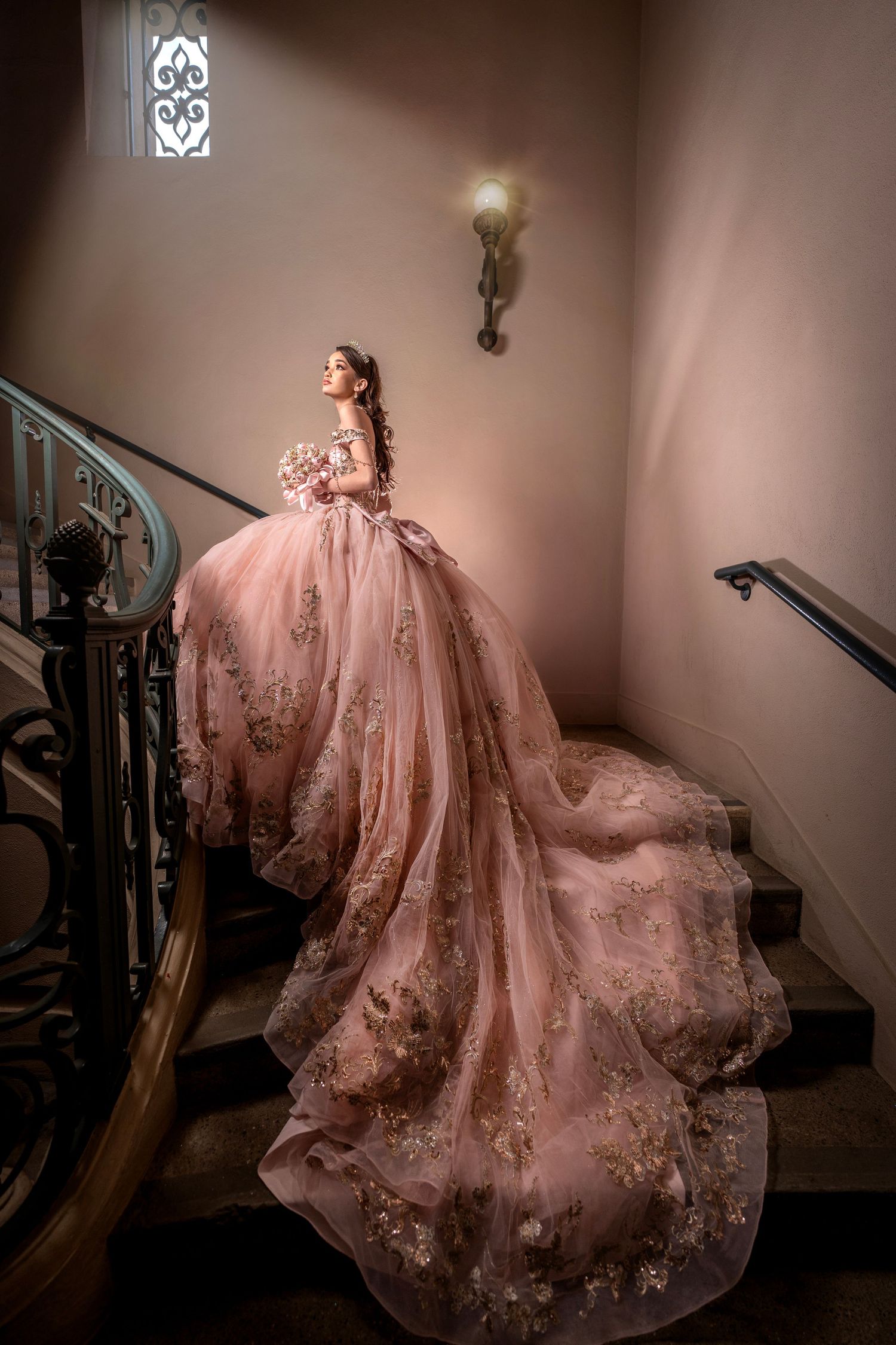 Figure in a flowing pink ball gown with floral details poses dramatically on a grand staircase in dim lighting.