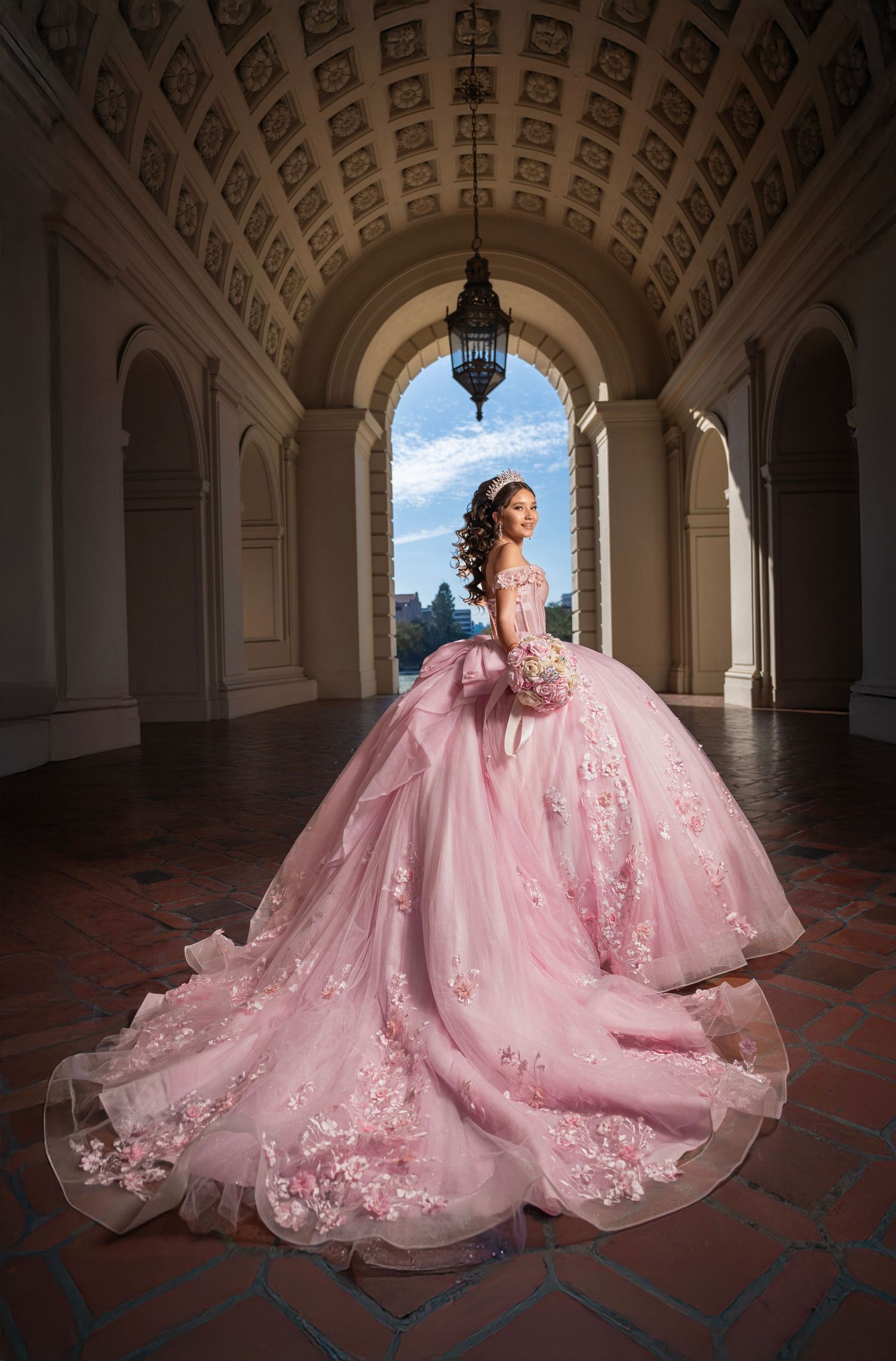 A pink princess ballgown with lace details and long train photographed in an ornate archway with vaulted ceiling.