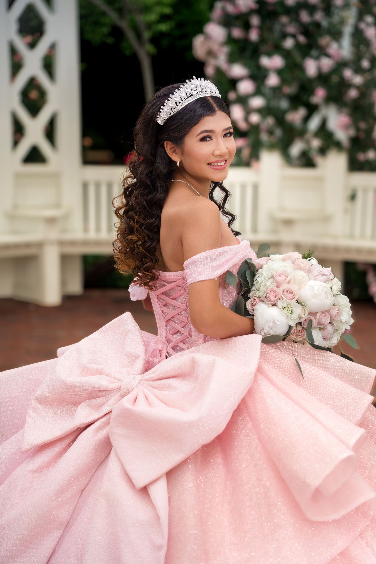 A quinceañera celebration featuring an elegant pink ball gown with corset back and sparkling tiara holding a floral bouquet.