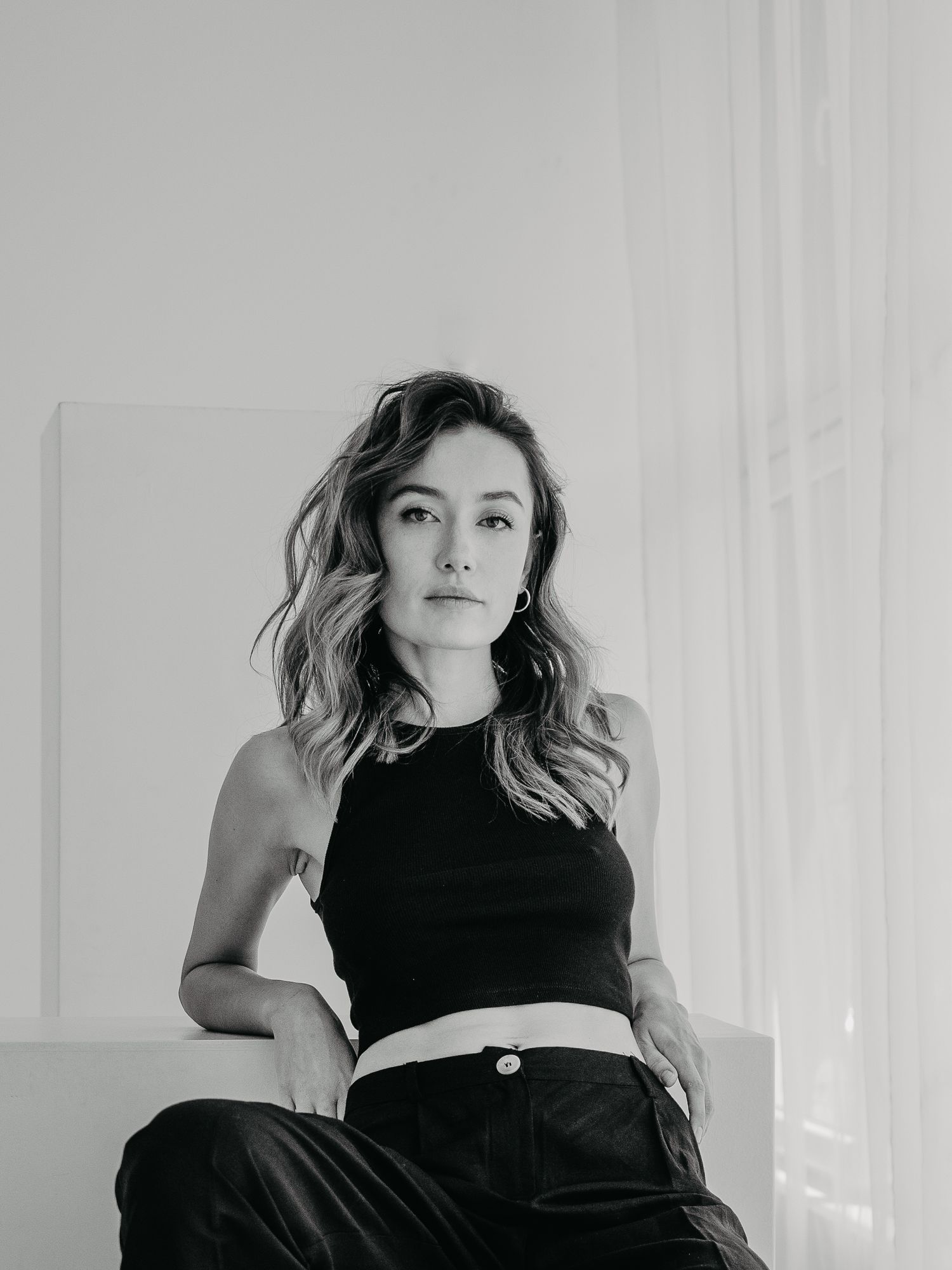 Woman with wavy hair in black top and pants sitting down on white stairs