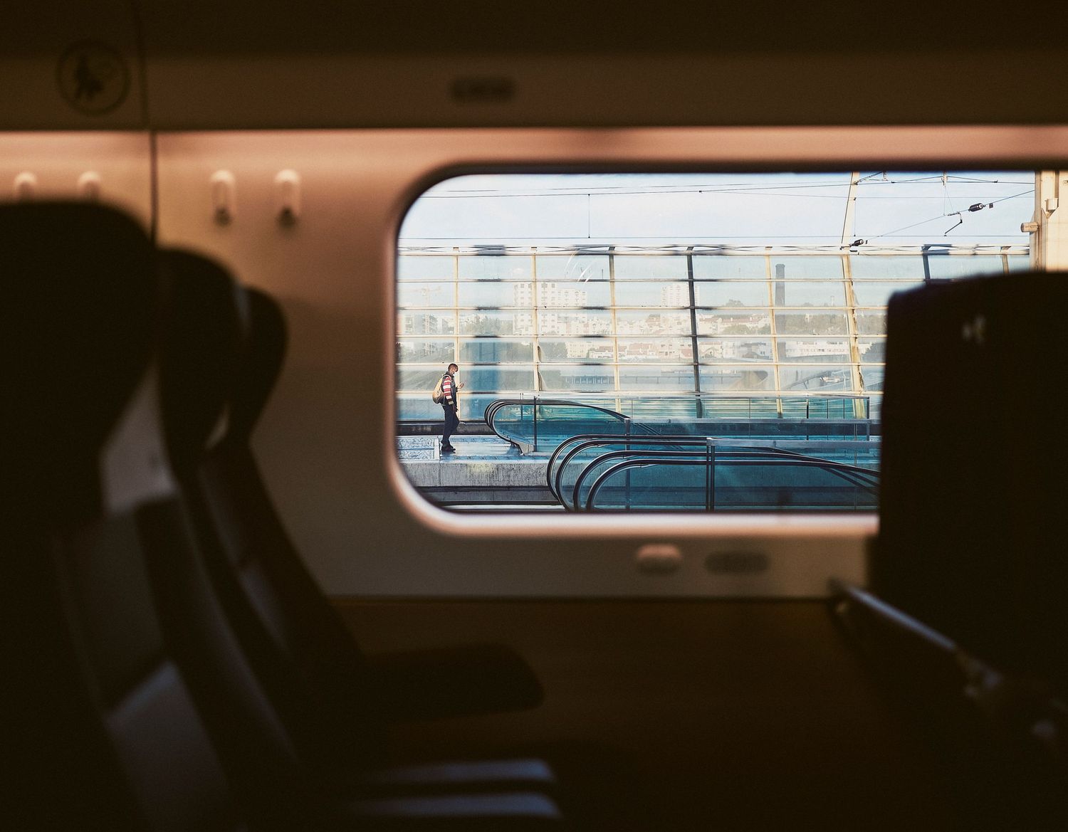 View through train window shows silhouetted seats against bright industrial landscape outside.