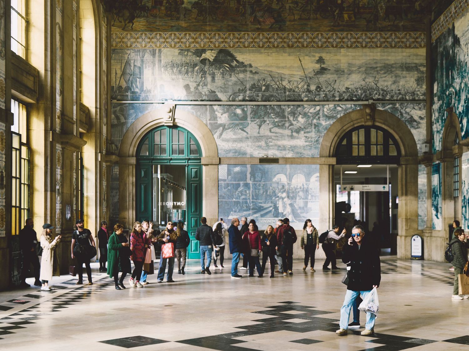 Historic railway station interior with blue azulejo tile walls and ornate decor as visitors gather in Porto, Portugal.