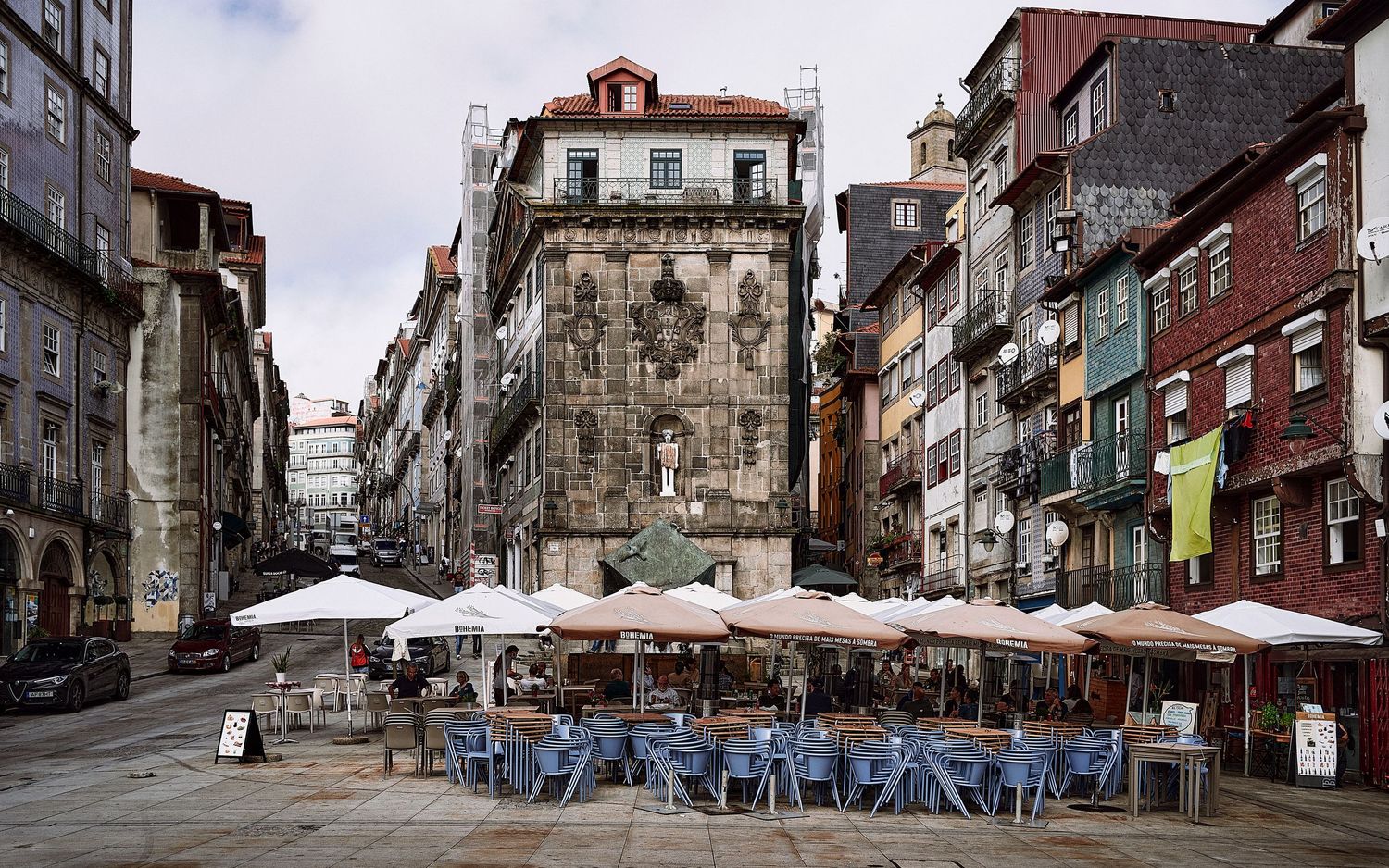 Historic Porto street with outdoor cafe tables beneath umbrellas surrounded by traditional Portuguese architecture.
