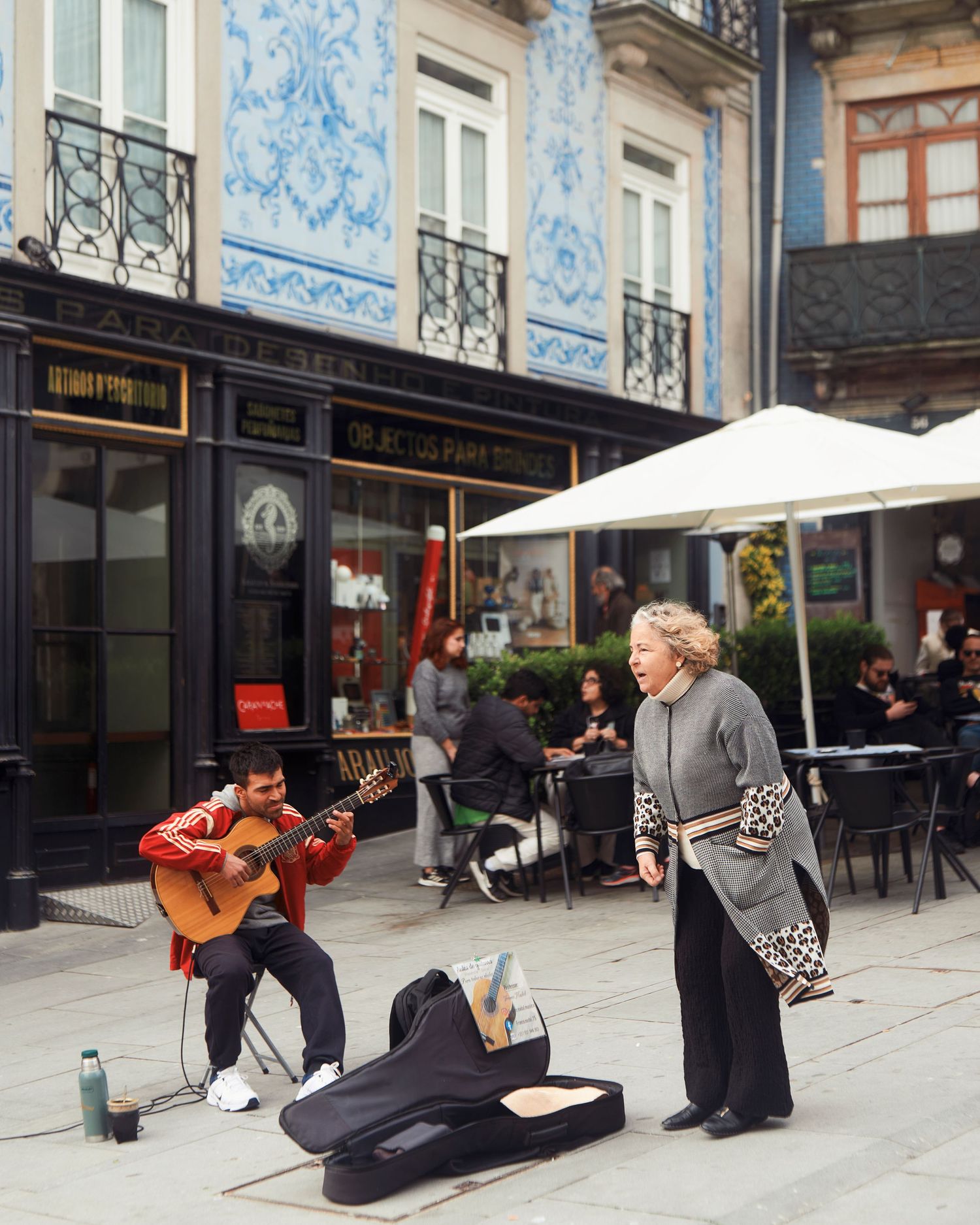 Street musicians perform outside a cafe with traditional architecture and blue tile facade in Porto.