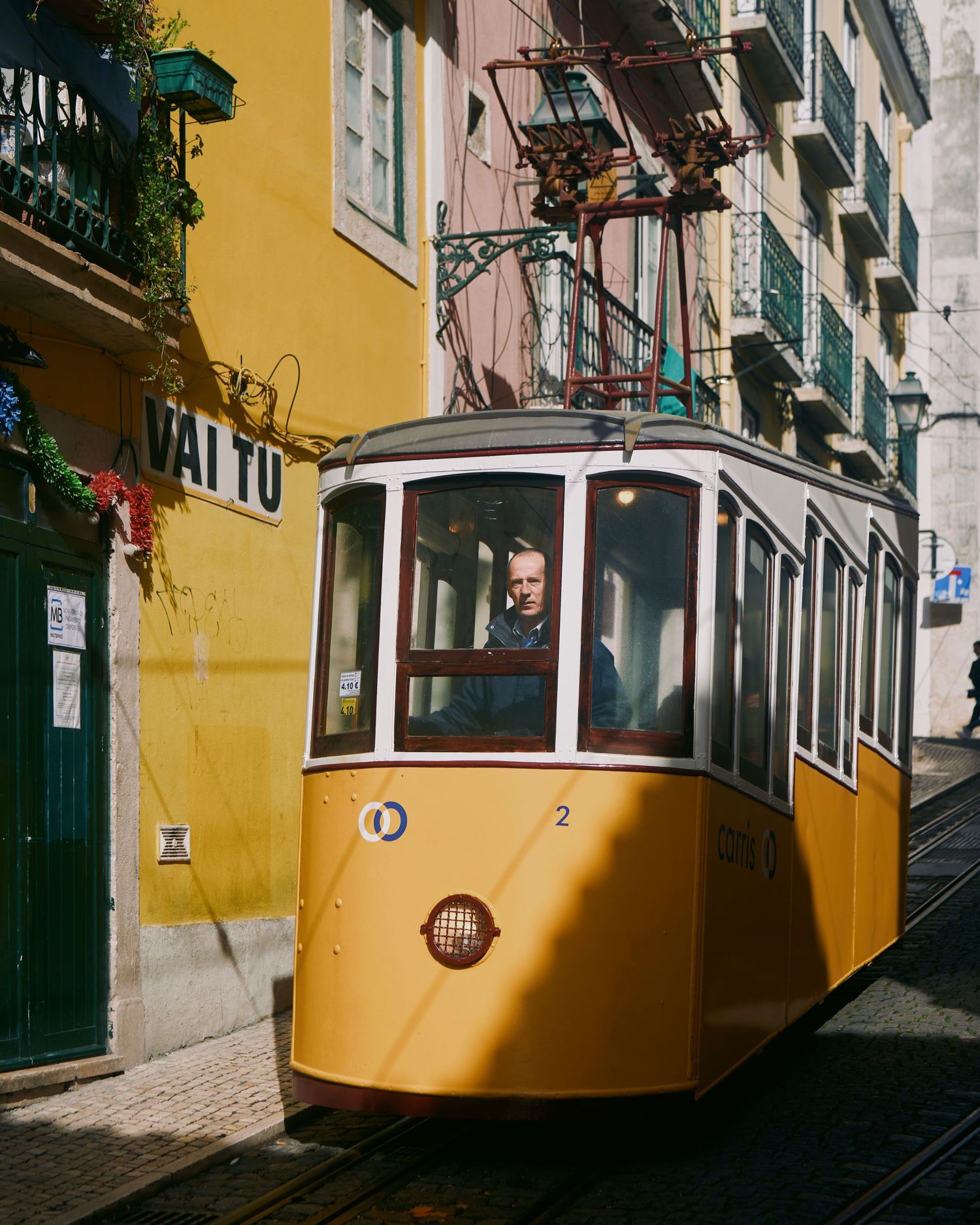 Vintage yellow tram car travels through narrow street between colorful buildings in Lisbon, Portugal.