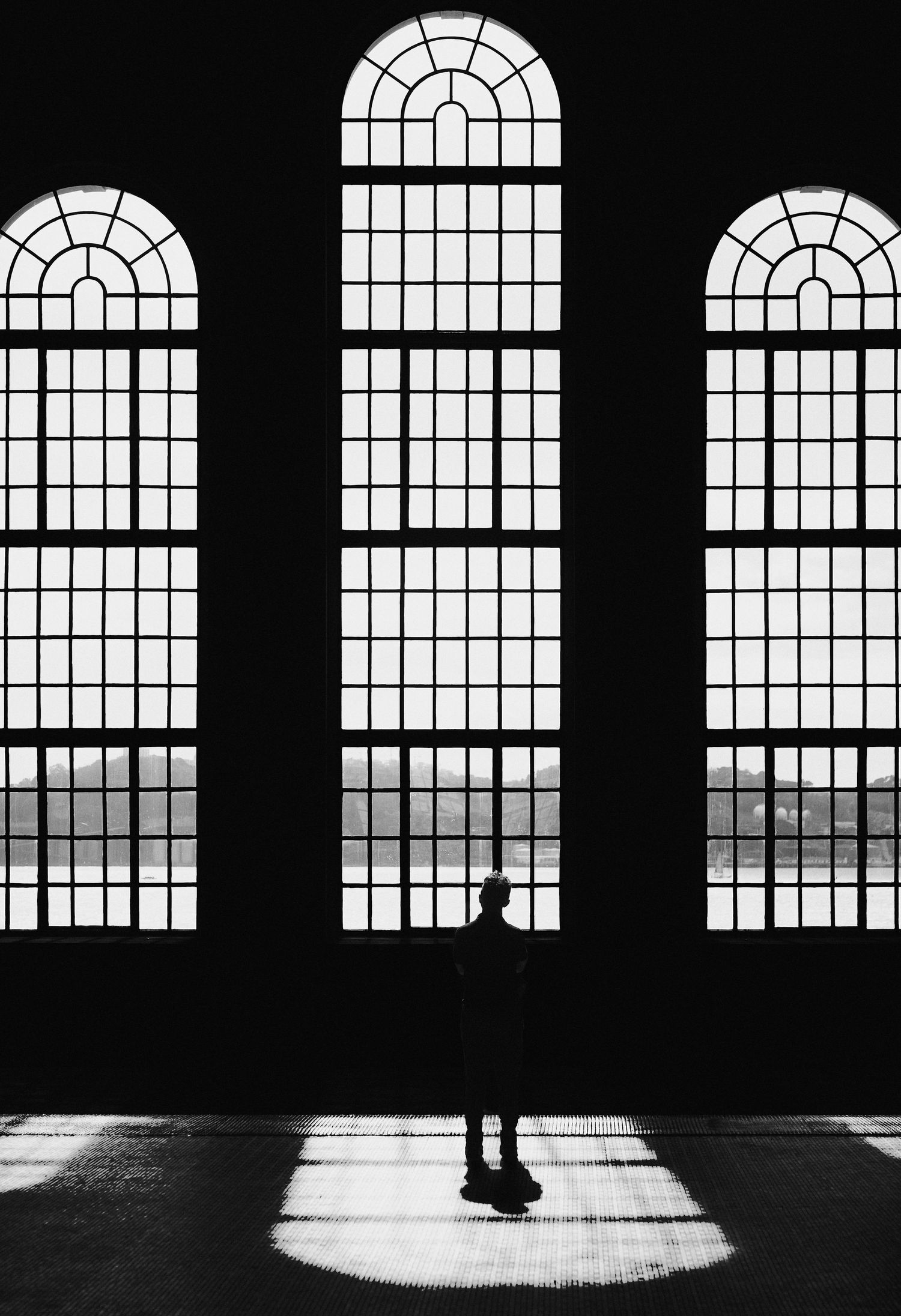A silhouetted figure stands in front of tall arched church windows casting dramatic shadows on the floor.