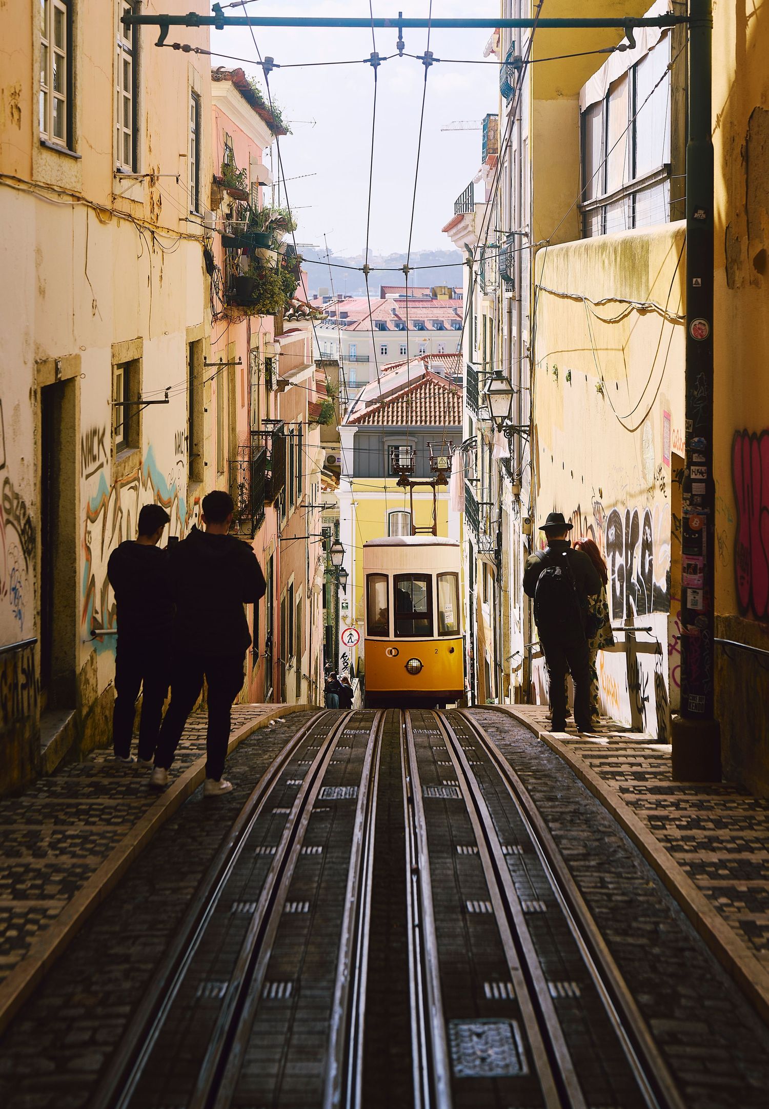 Yellow funicular tram ascending steep cobblestone street in Lisbon's historic Bica neighborhood with city views below.