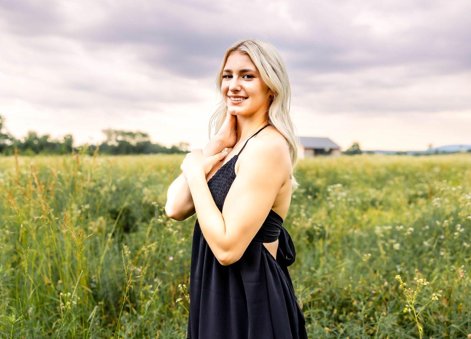Lifestyle fashion photo of a black dress against a cloudy summer sky and green field.