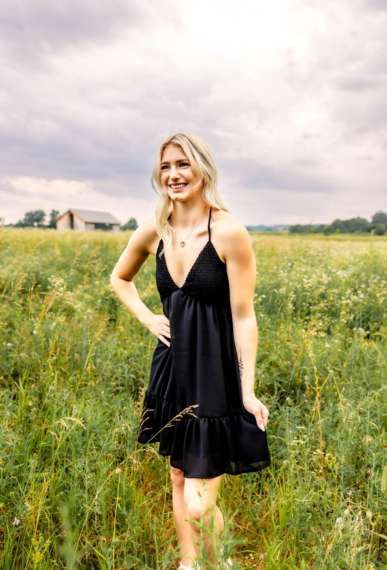 Black sundress with ruffle hem photographed in a flowering field under cloudy skies.