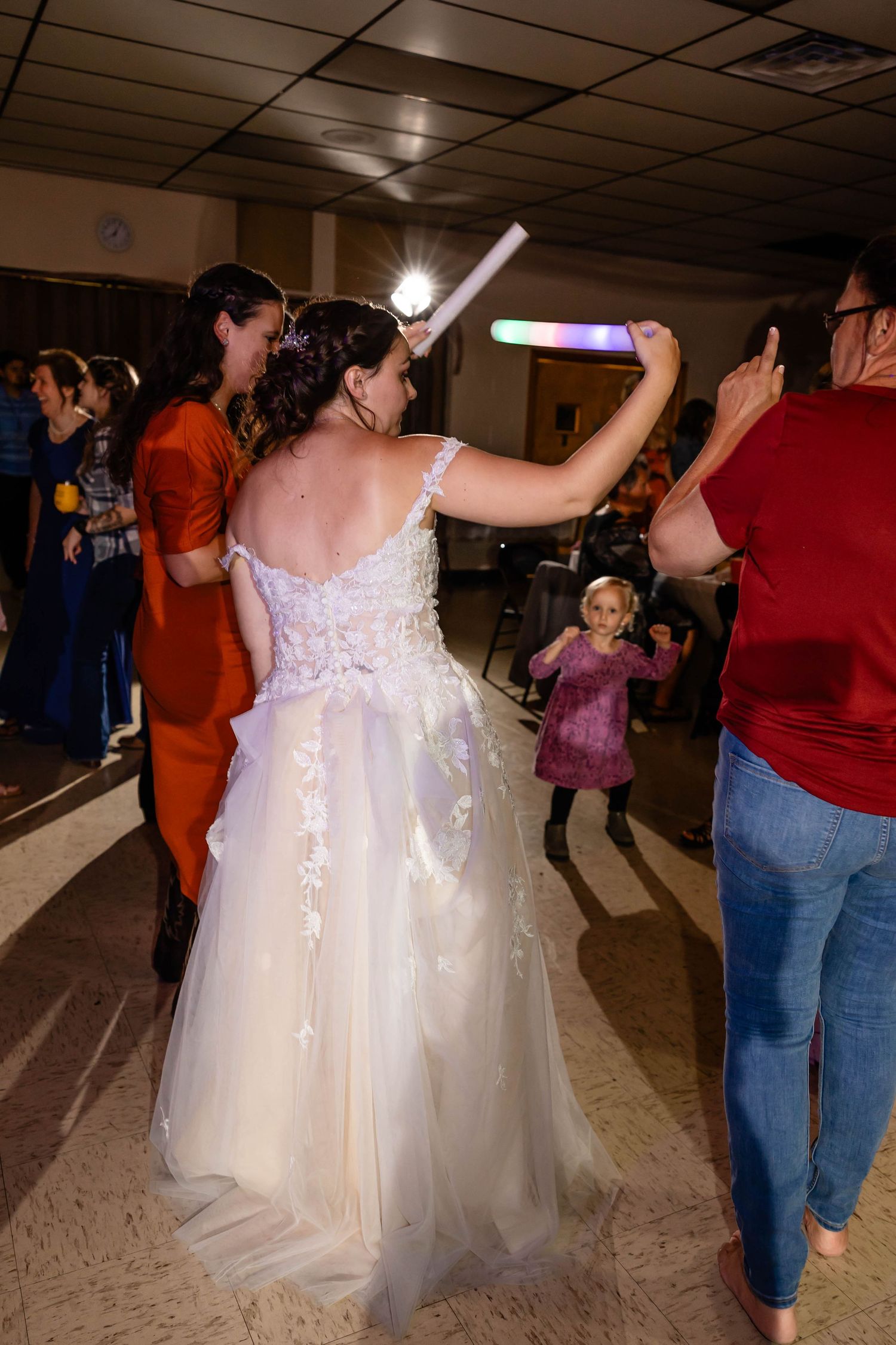 Bride in flowing lace gown dances with light-up party favors during reception celebration.