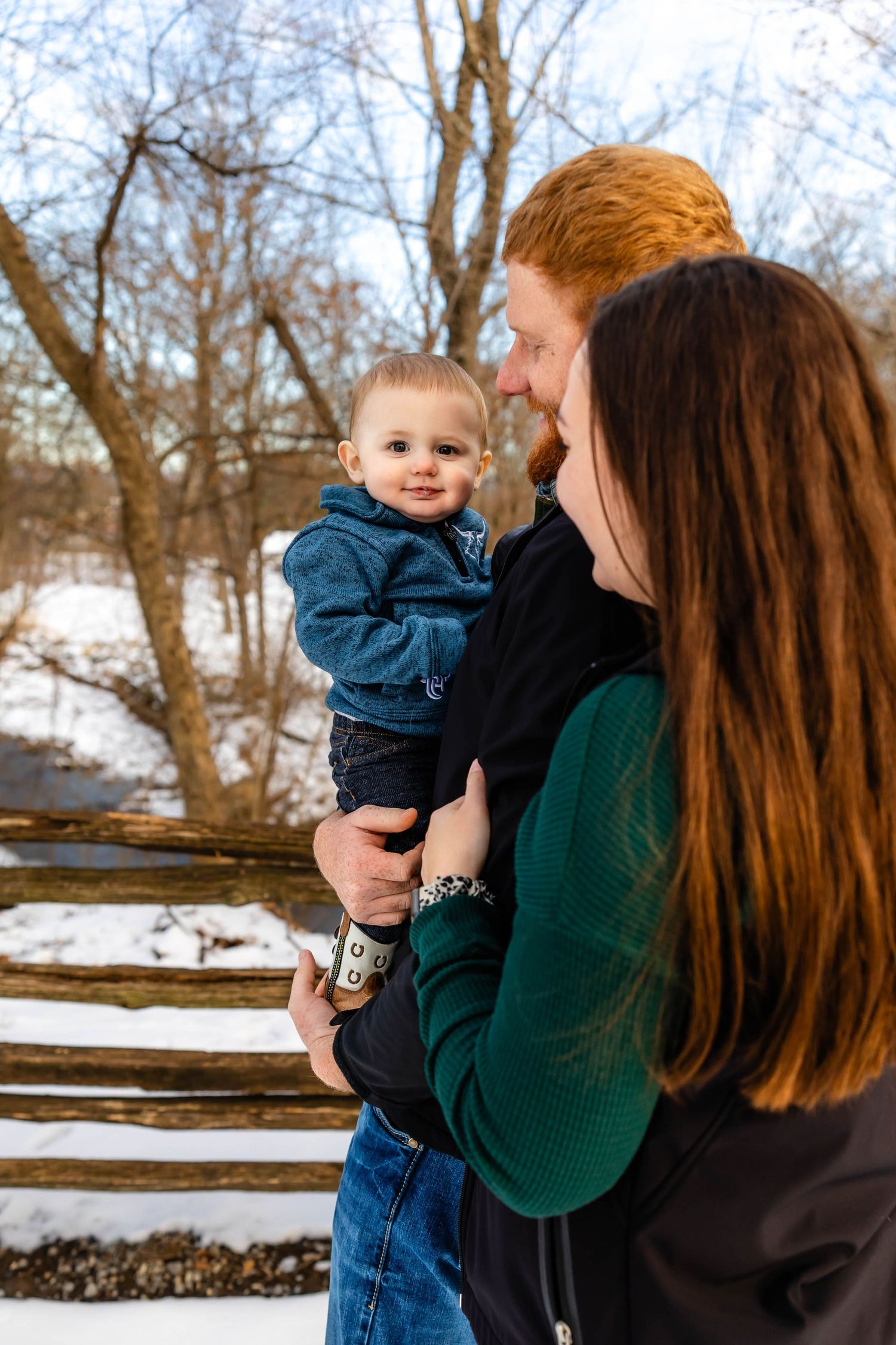 Sweet family interaction on winter day with snow-covered split rail fence in background.