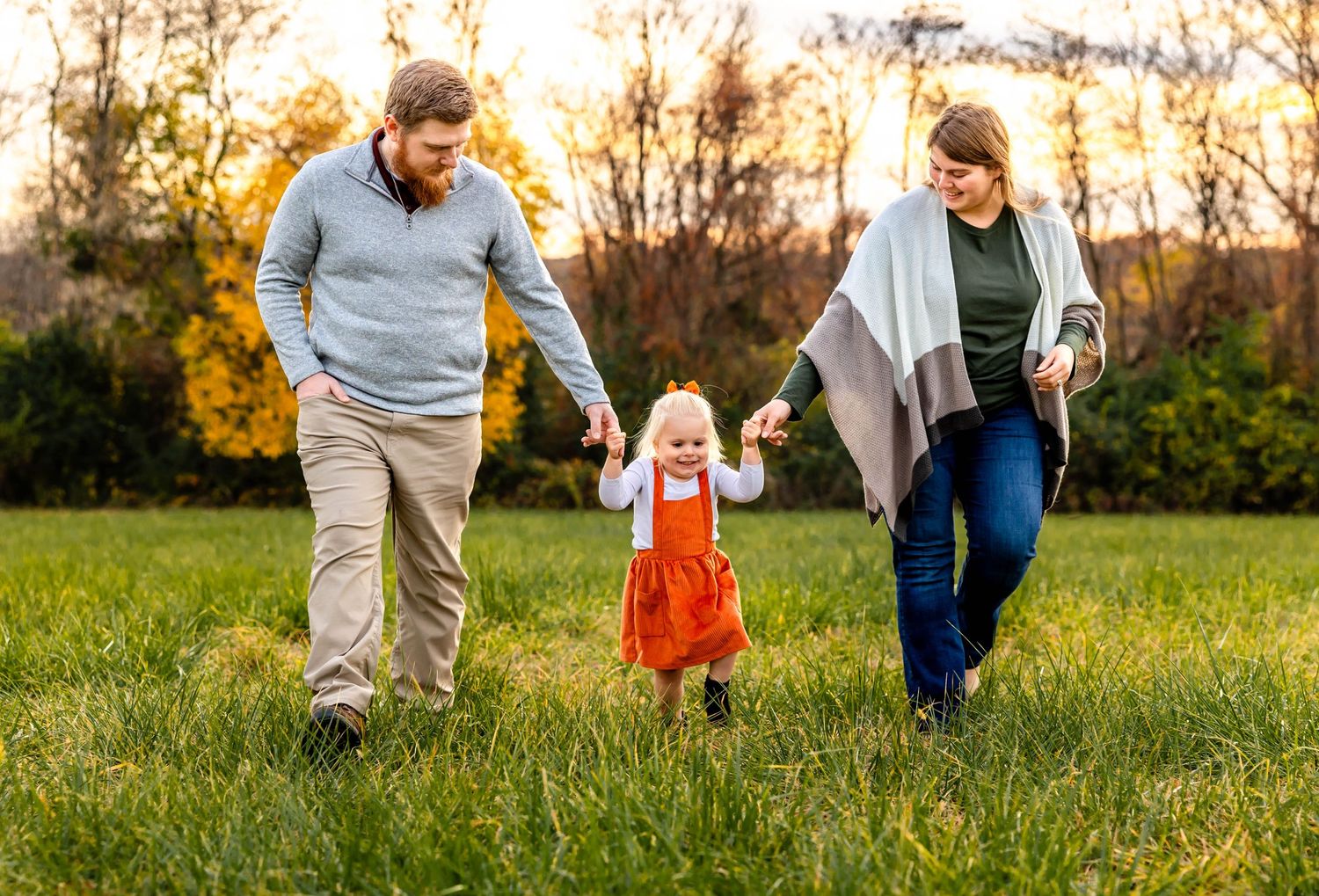 Happy family walking together through a grassy field at sunset.