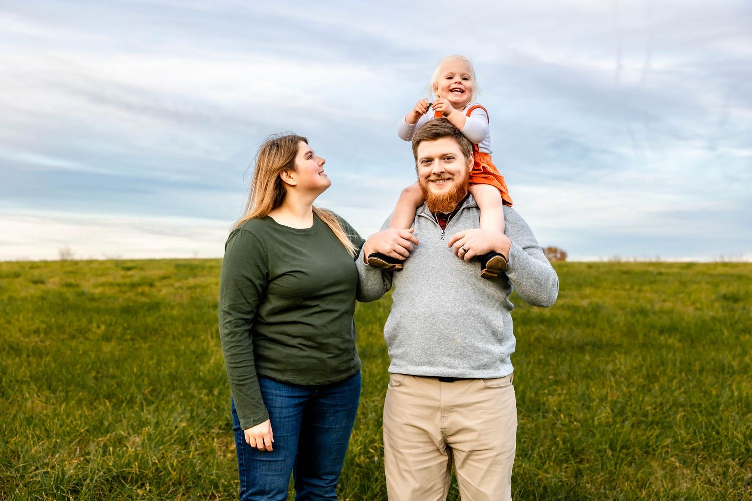 A joyful family moment captured outdoors in a green field under blue skies.